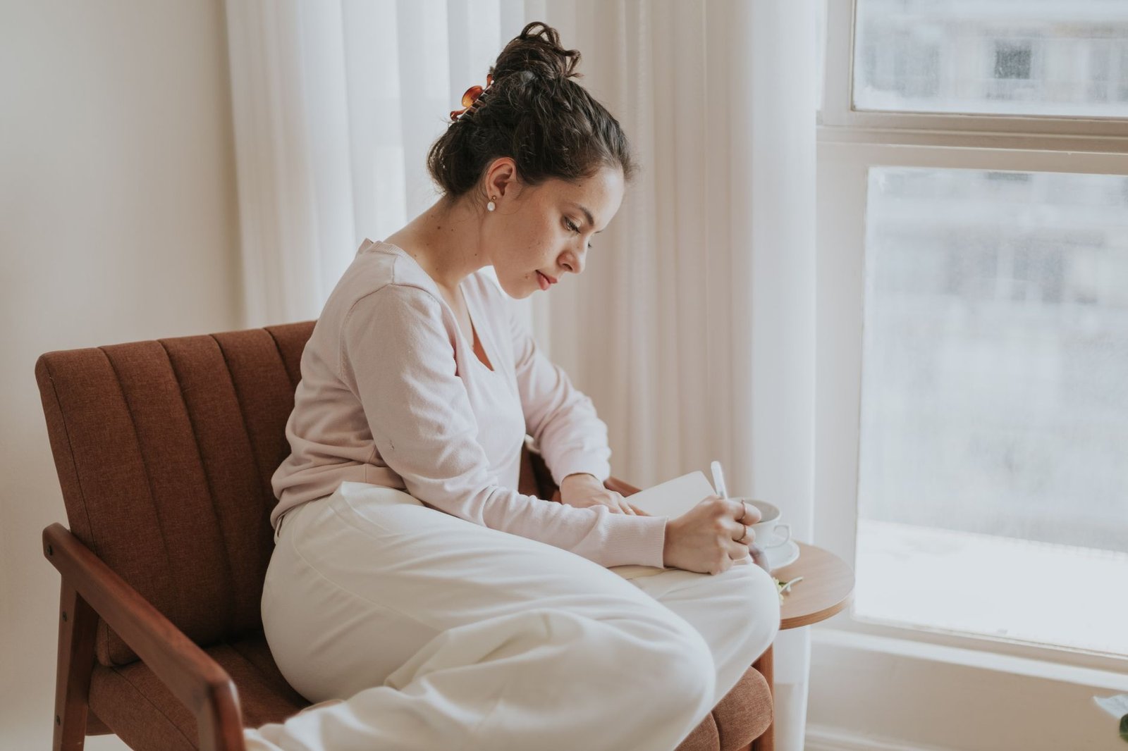 Mujer escribiendo un diario emocional junto a la ventana para reconocer sus emociones
