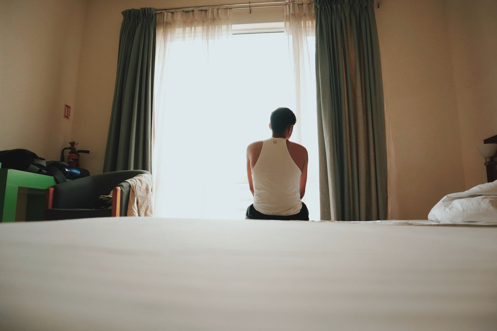 Persona sentada en el borde de la cama mirando por la ventana, señal de sentirse perdido